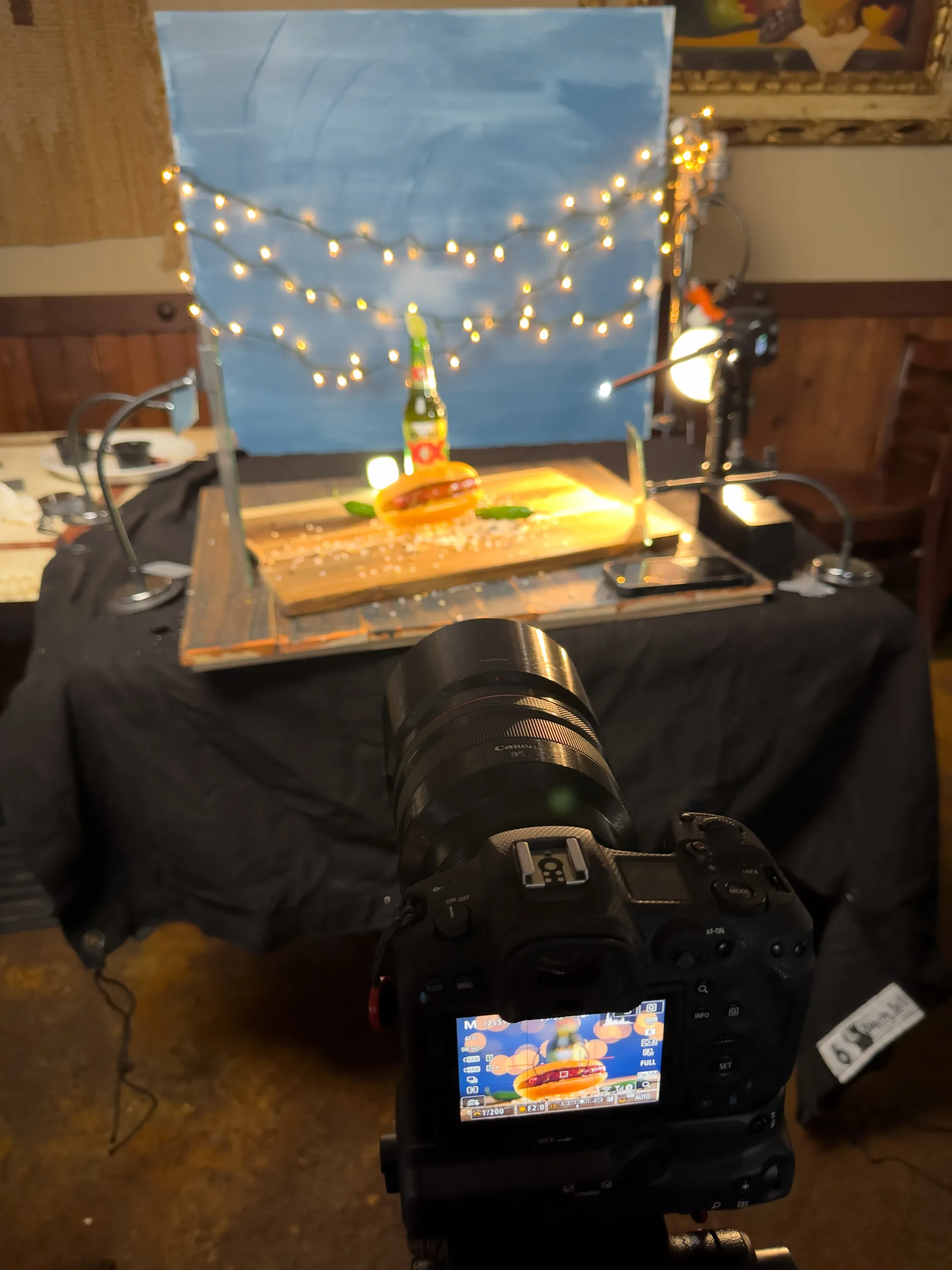 Product shoot setup with a blue backdrop, string lights and a camera on a tabletop set - Raging Bull Food Photography