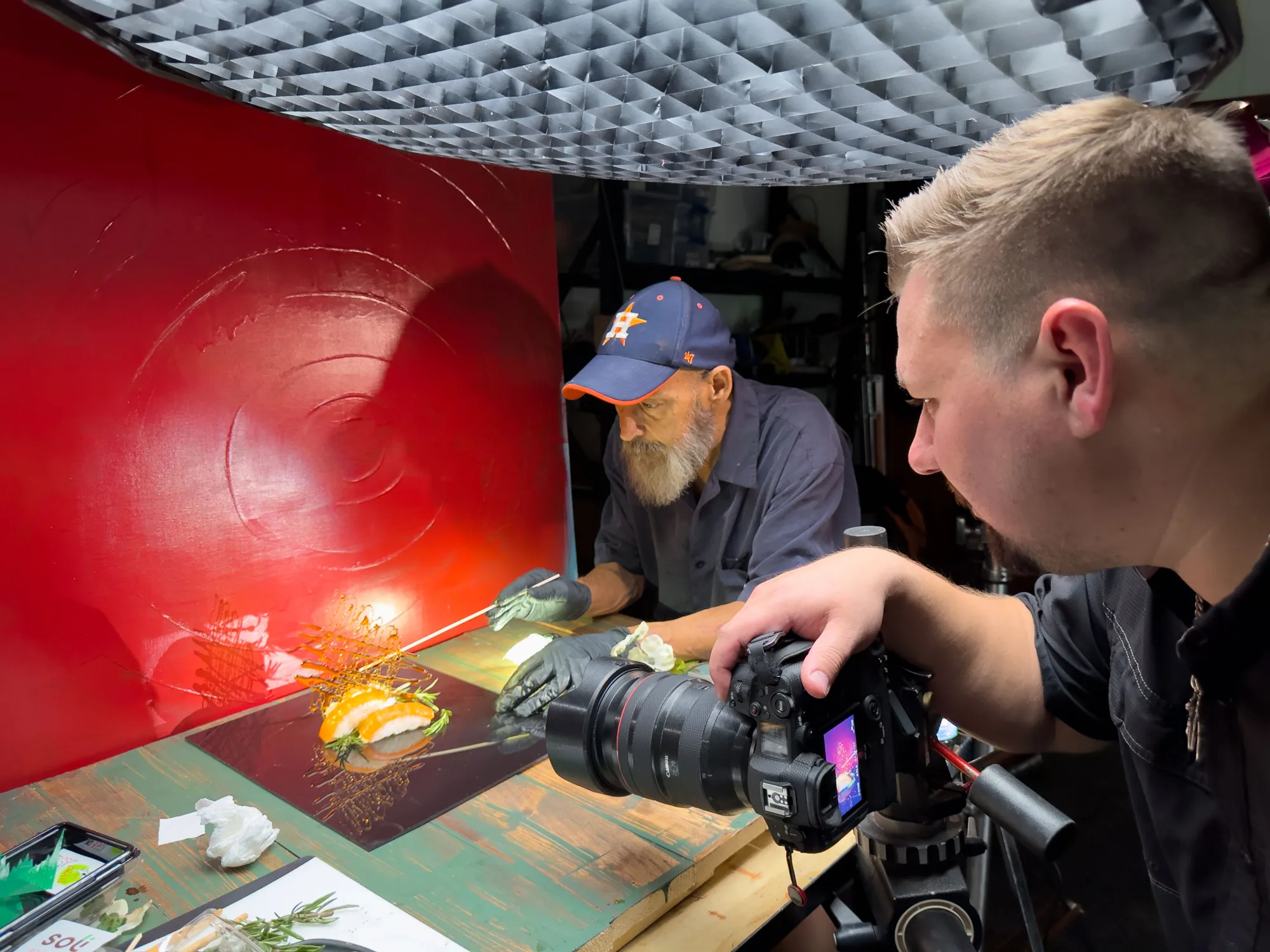 Two-person crew adjusting camera gear beside a red-lit studio backdrop on a food shoot - Raging Bull Food Photography