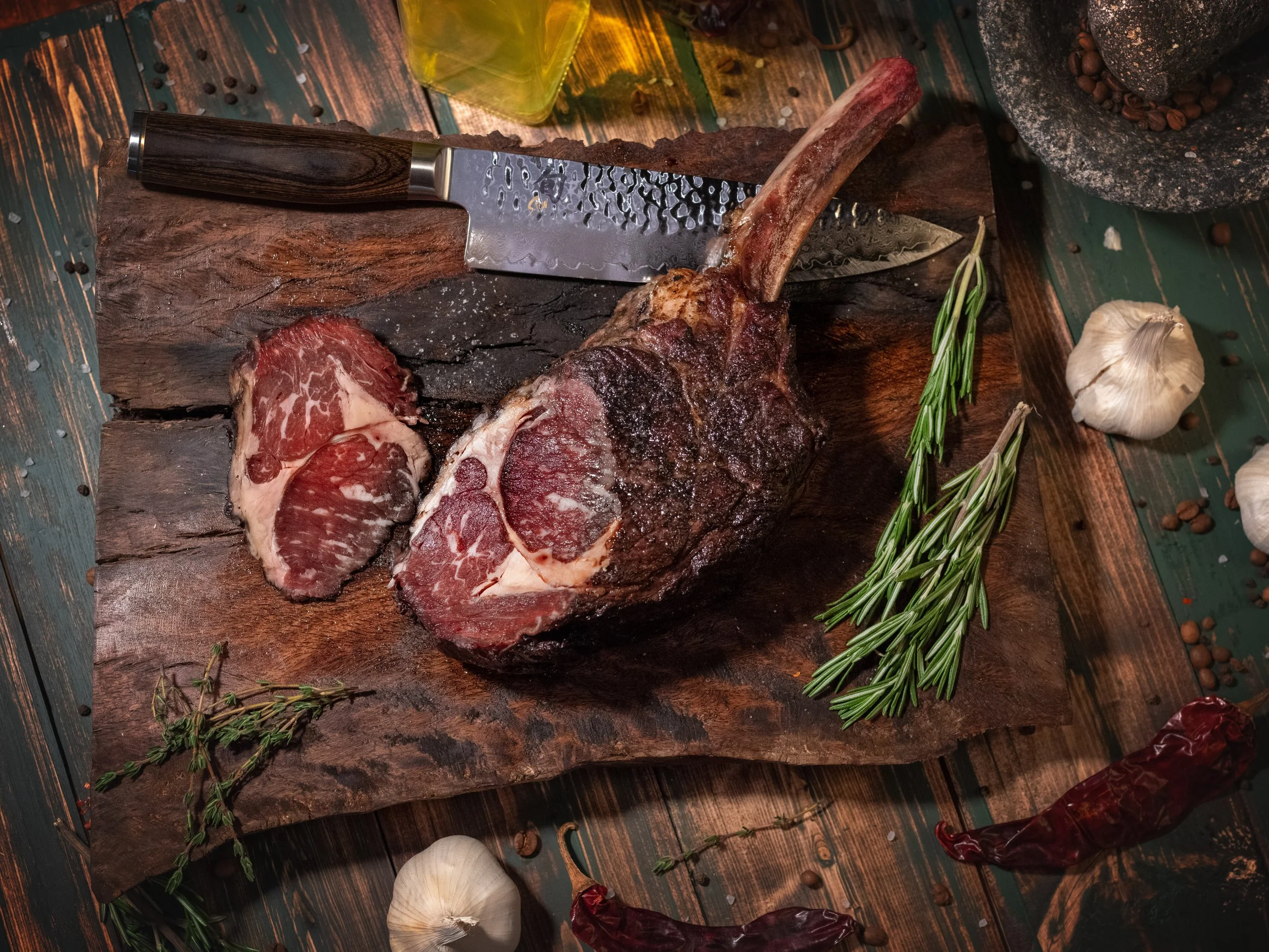 Sliced tomahawk steak on a cutting board with rosemary and garlic