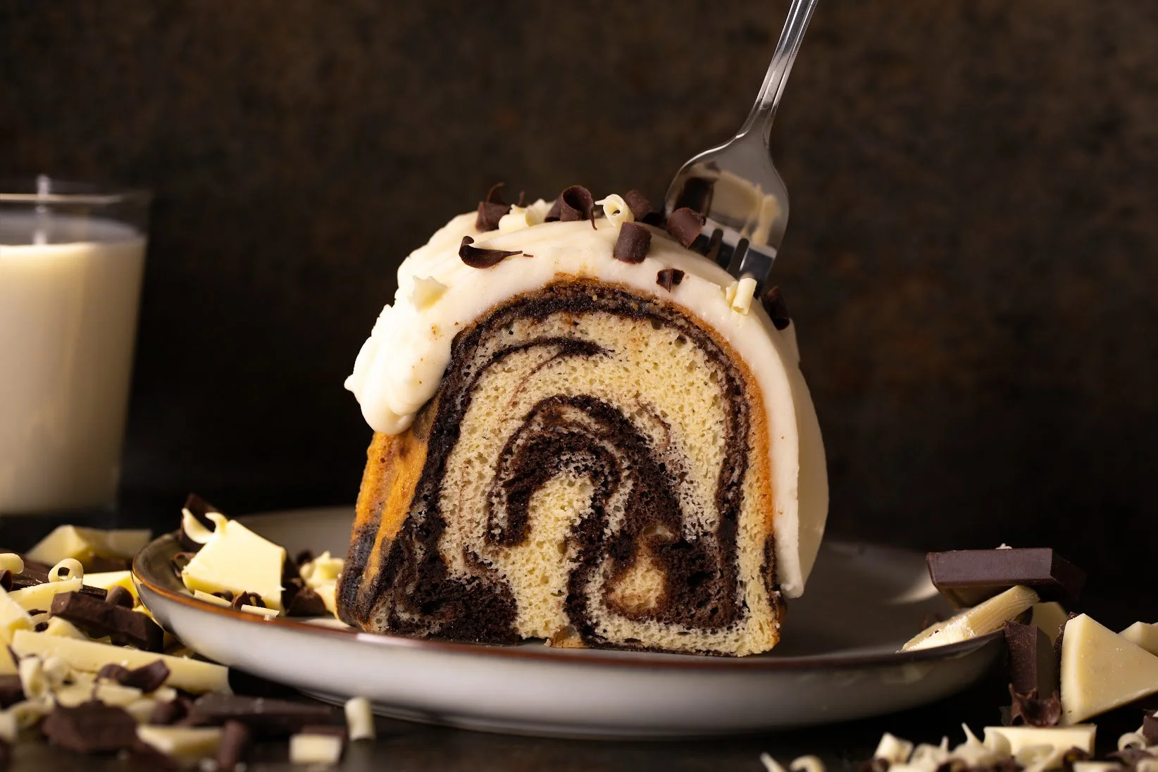 Slice of chocolate swirl cake with a fork and a glass of milk