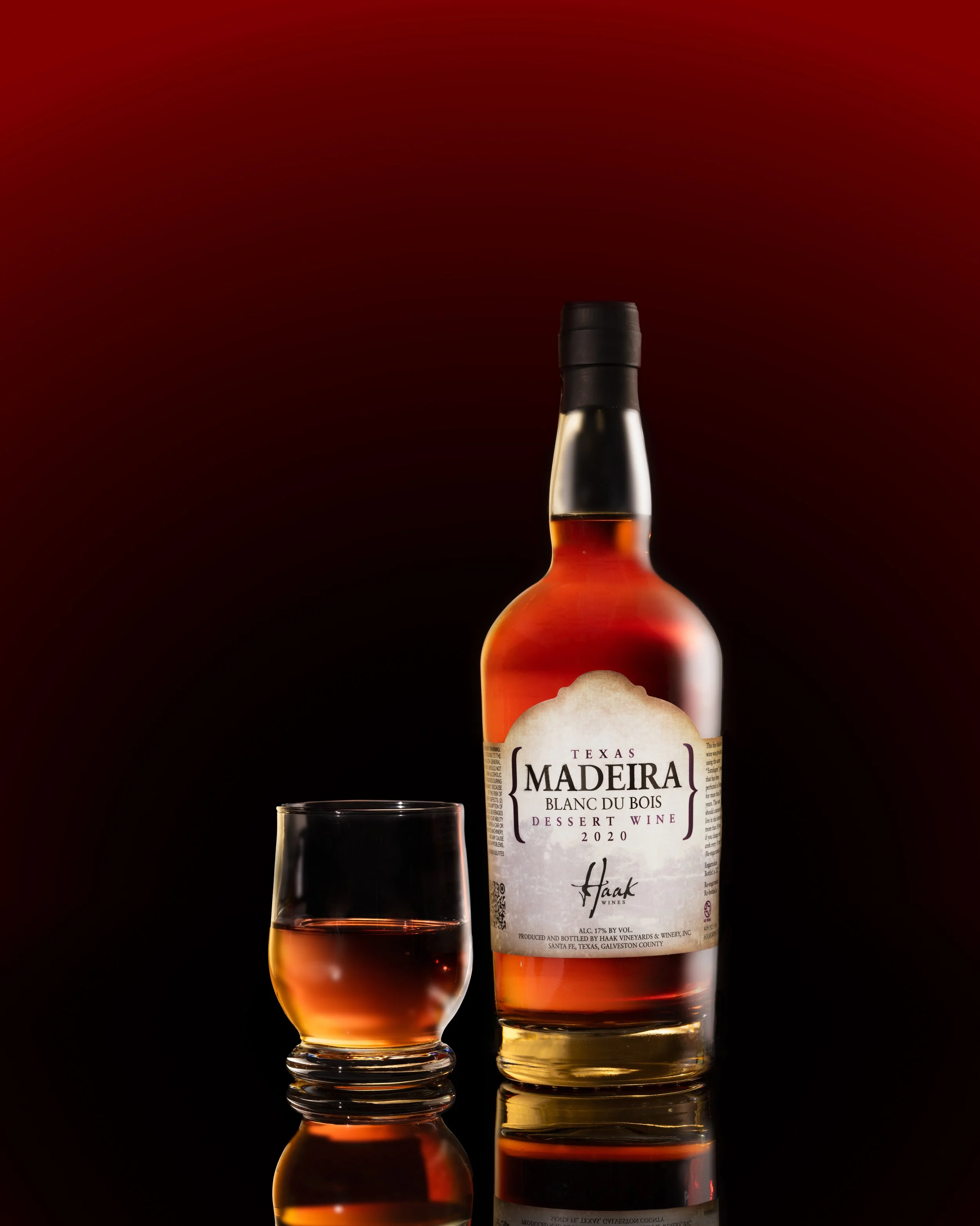 Madeira dessert wine bottle and glass against a deep red background