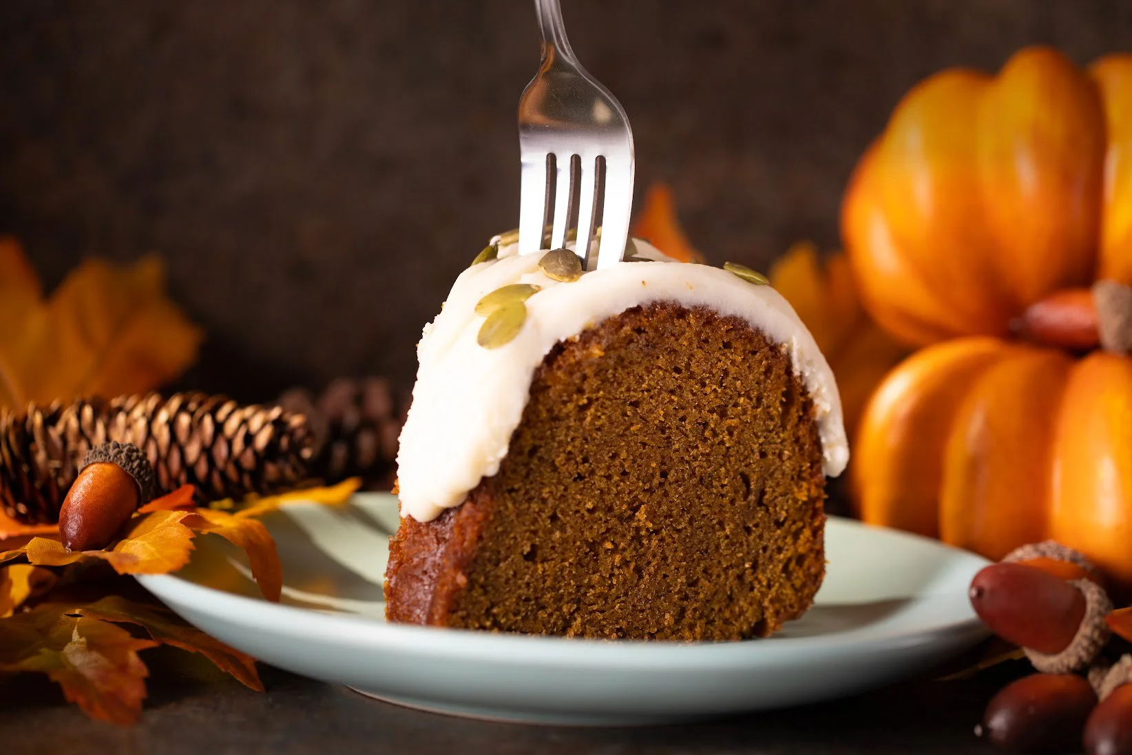 Pumpkin bundt cake with cream glaze among autumn leaves and pumpkins