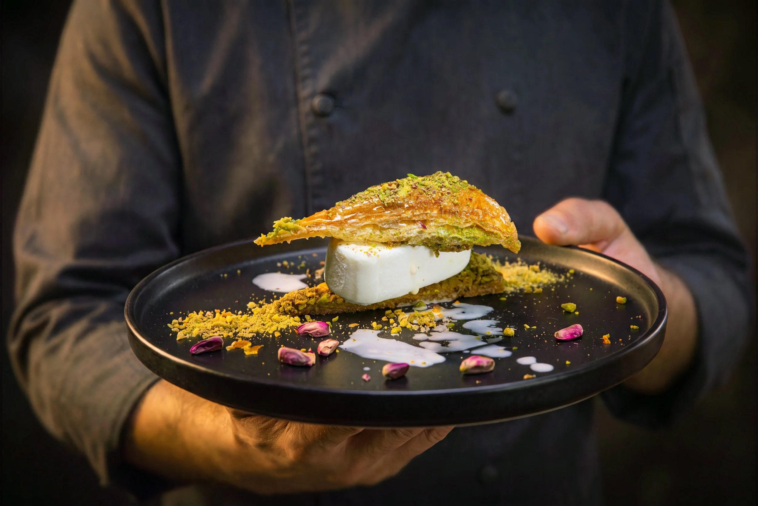 Chef holding a plate of baklava with ice cream and pistachios