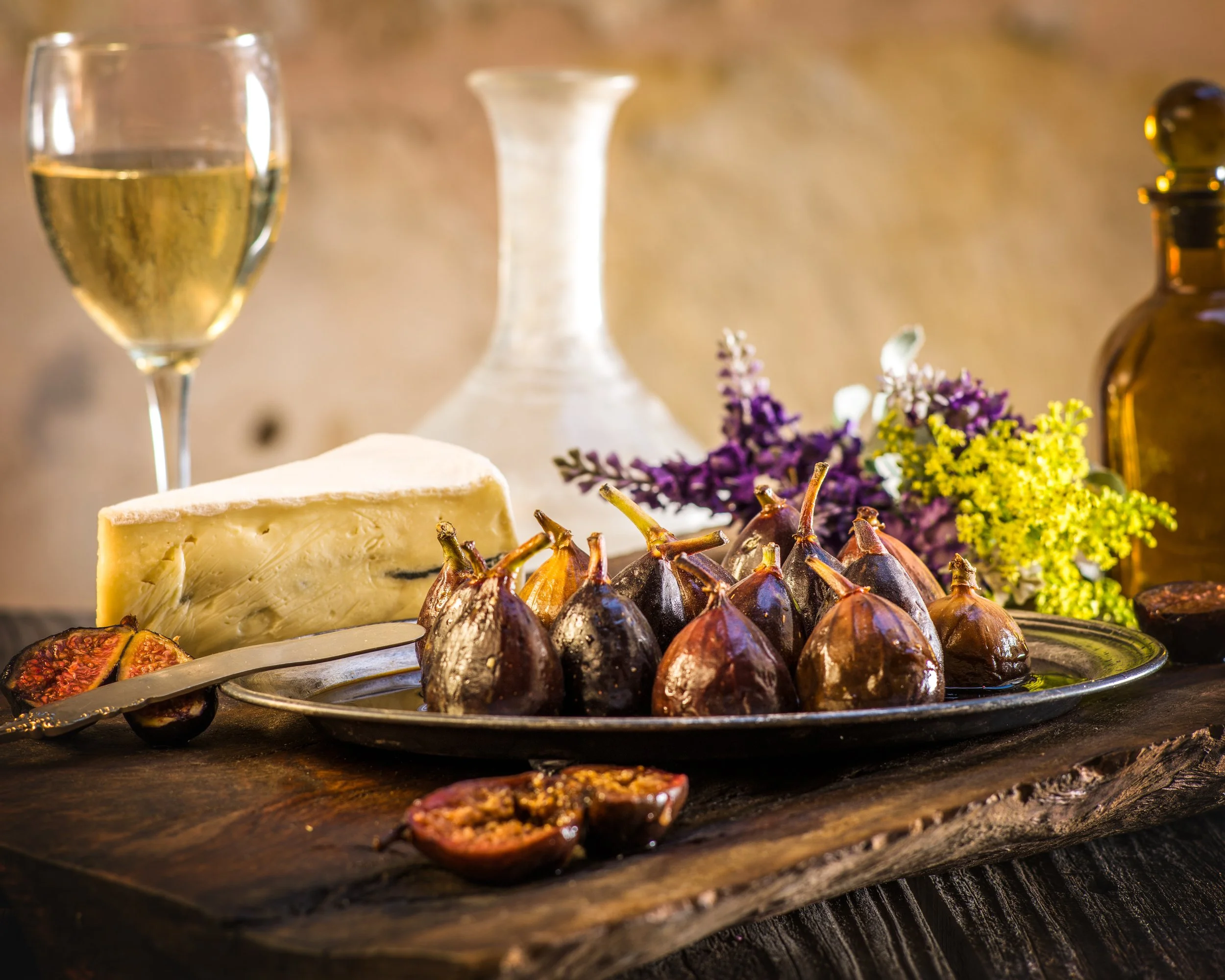Roasted figs on a plate with brie, flowers, and a glass of white wine
