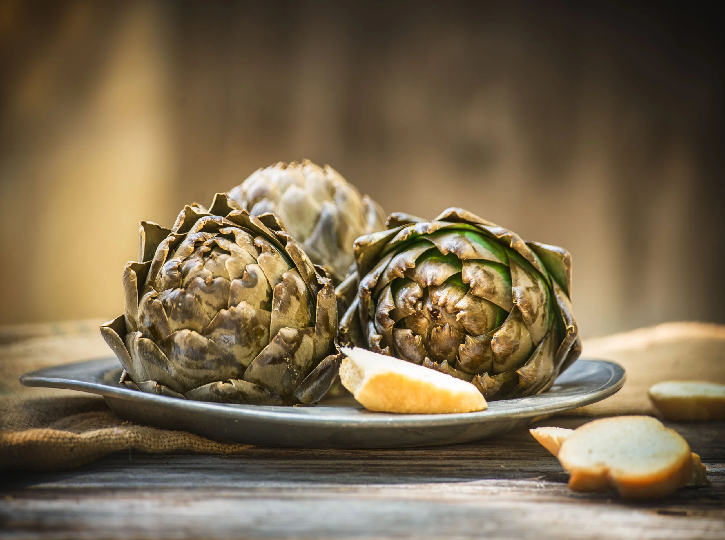 Three artichokes with a lemon wedge on a pewter platter