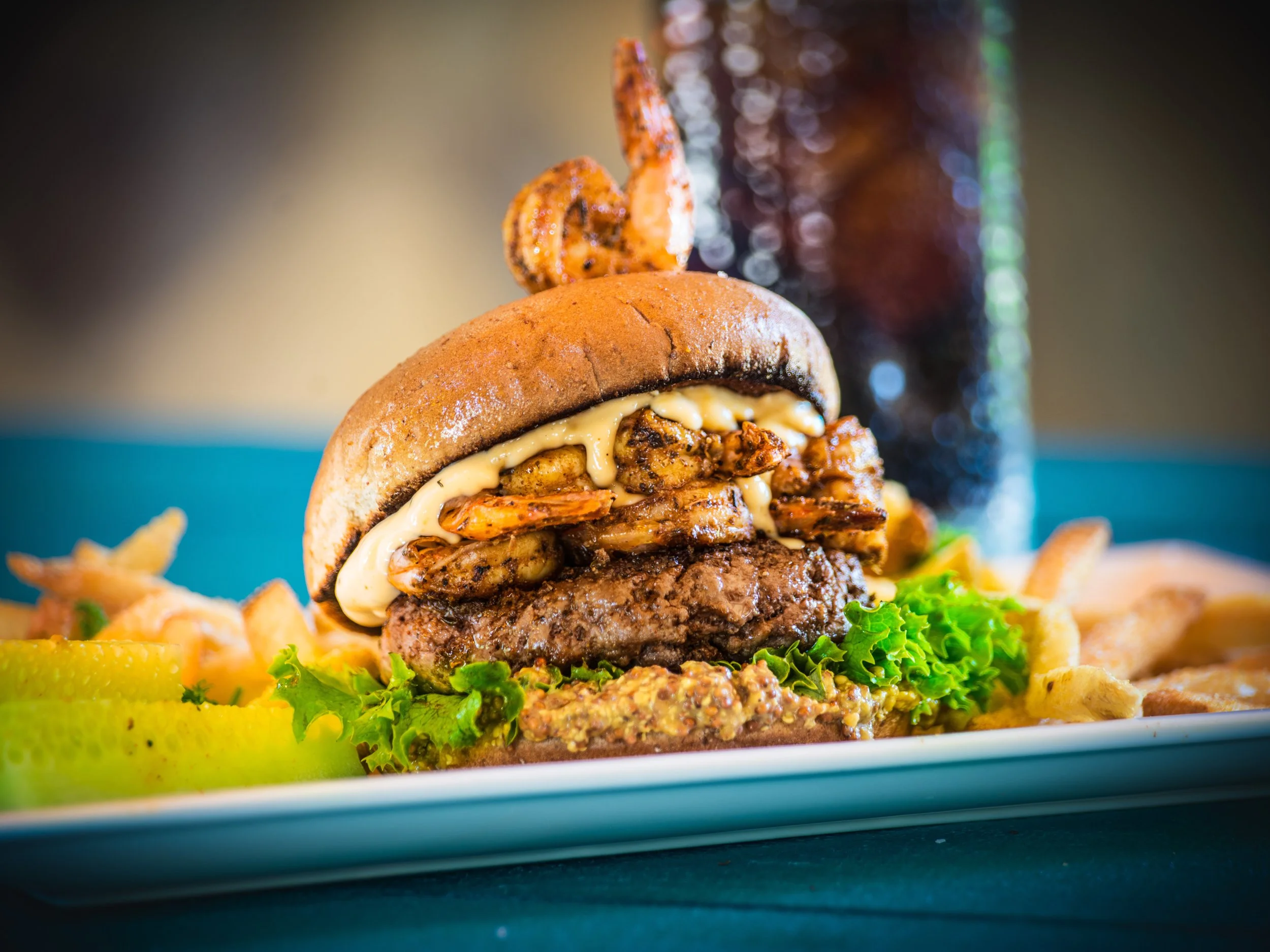 Burger topped with fried shrimp served with fries on a blue plate
