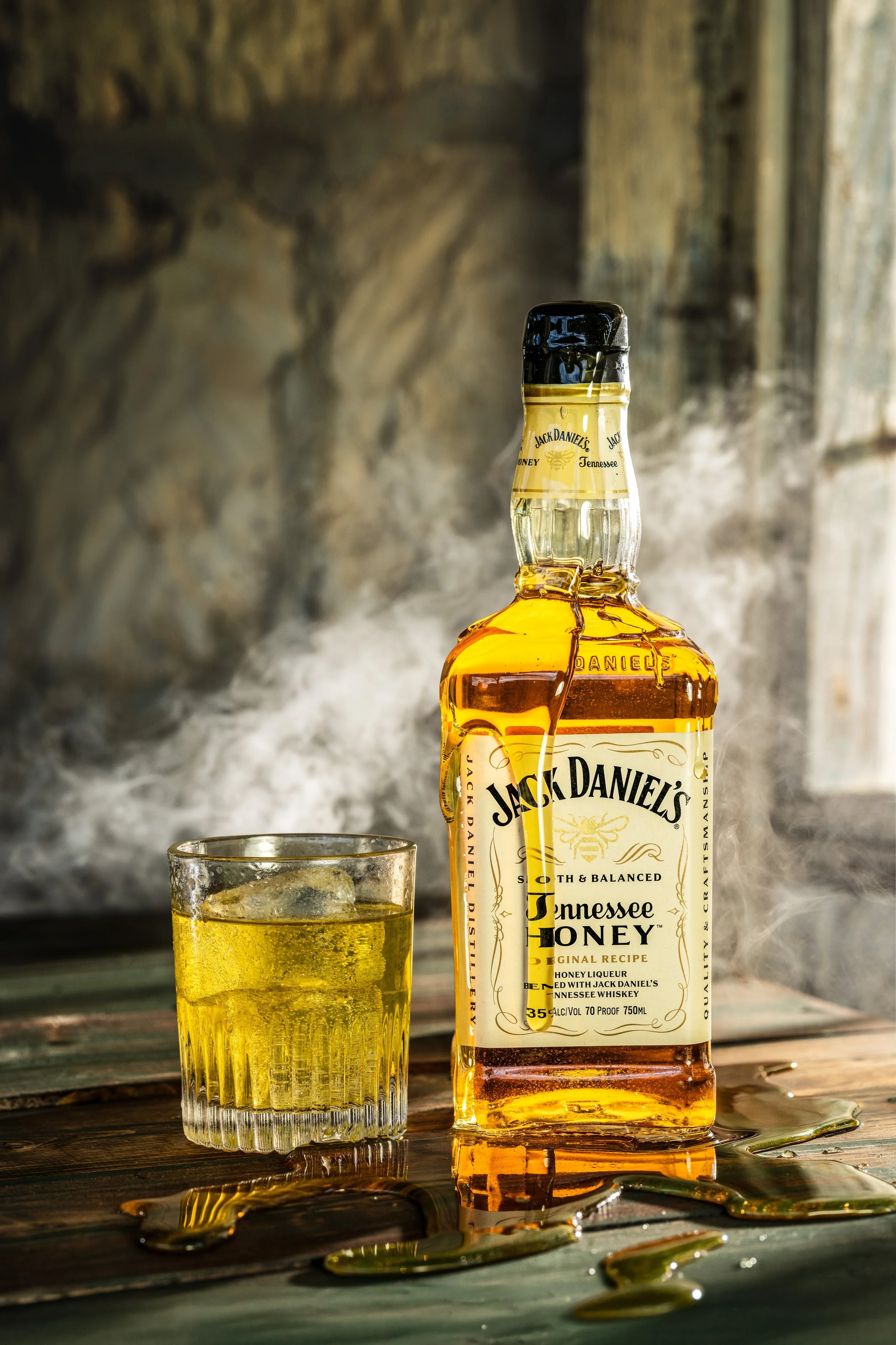 Jack Daniel's Tennessee Honey bottle and glass with honey and smoke