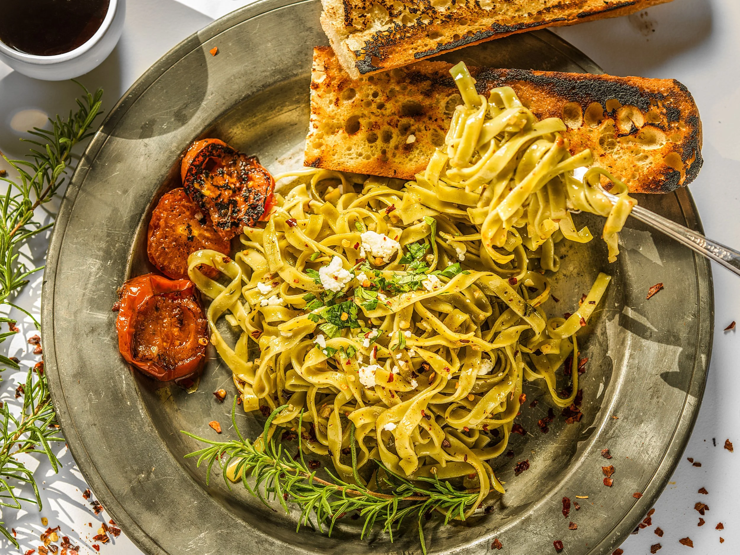 Fettuccine pasta with roasted tomatoes and grilled bread on a metal plate