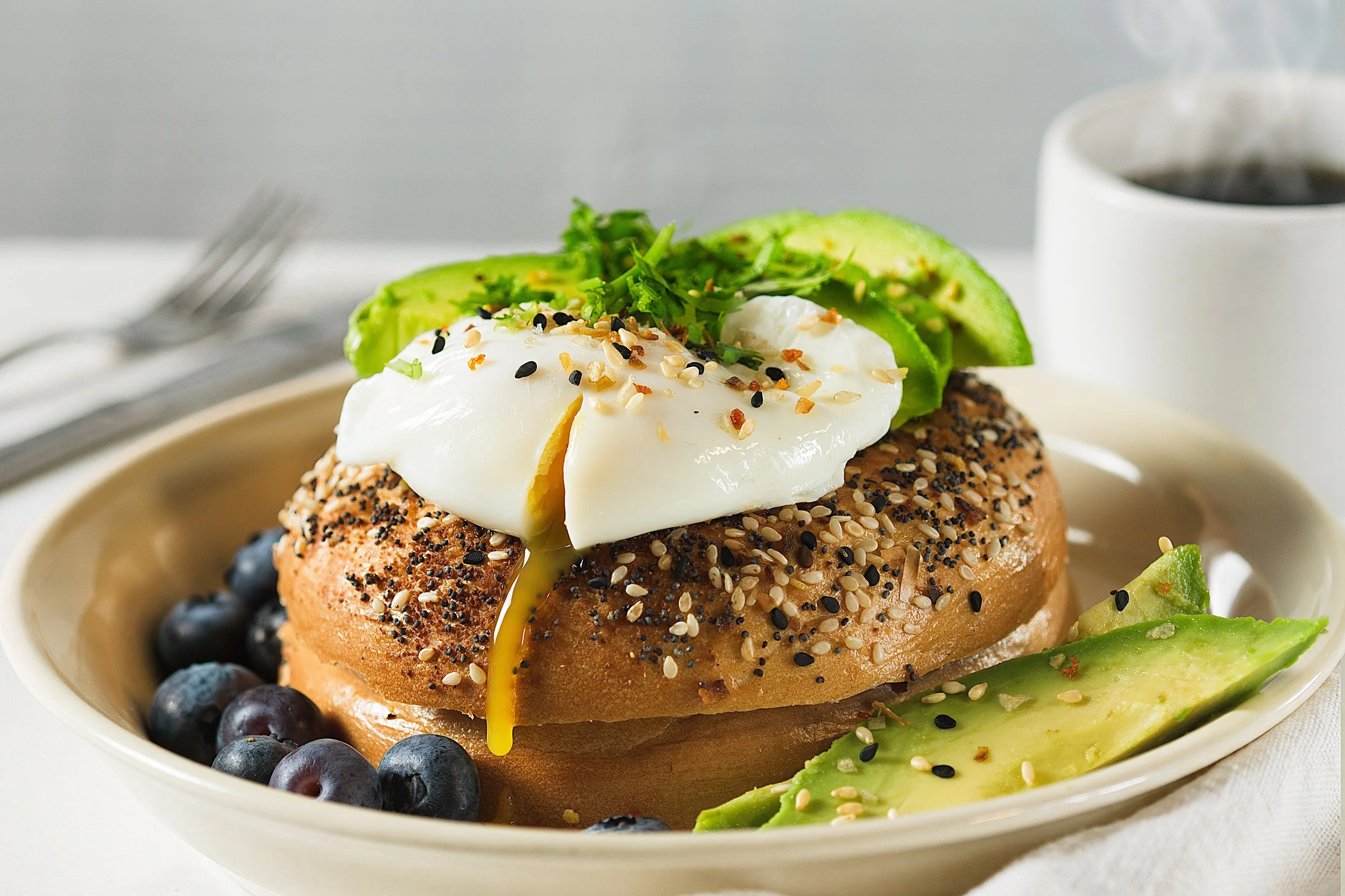 Poached egg and avocado on a seeded bagel with blueberries