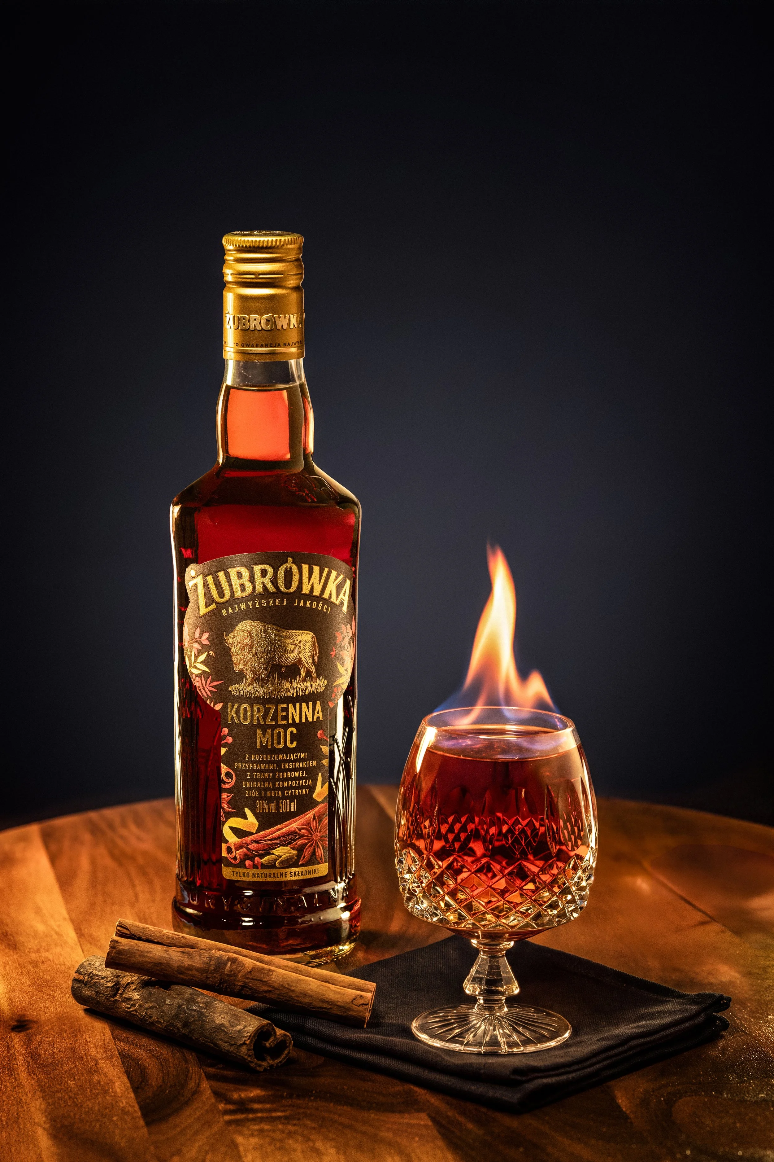 Zubrowka vodka bottle with a flaming glass of spiced liquor and cinnamon sticks