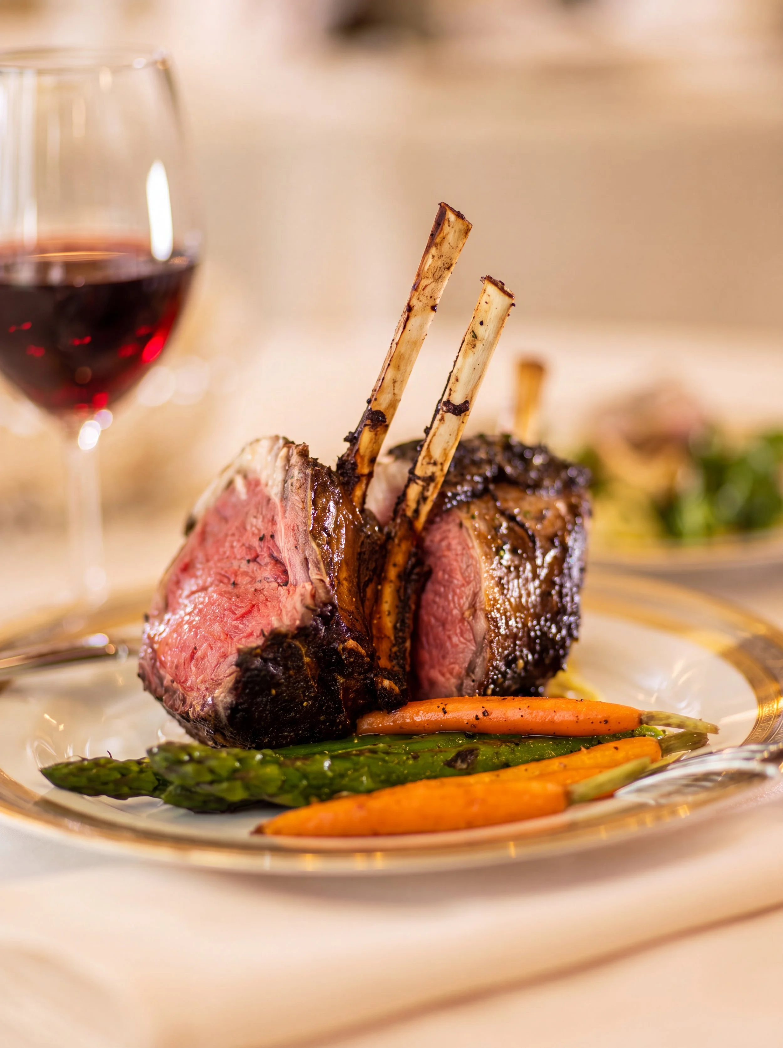 Sliced rack of lamb with carrots and asparagus beside a glass of red wine